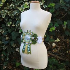 a white mannequin wearing a green and white sash with flowers on it's belt