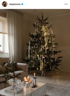 a living room with a lit christmas tree in the corner and candles on the coffee table