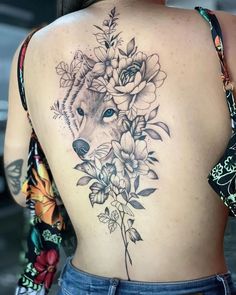 the back of a woman's body with flowers and a wolf tattoo on it