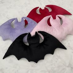 four different colors of bat shaped pillows on the snow covered ground, one is pink, one is purple and one is red