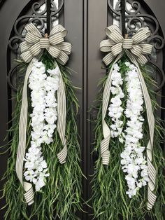 two wreaths decorated with white flowers and greenery are hanging on the front door