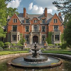 a large red brick house with a fountain in the foreground and trees surrounding it