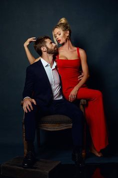 a man and woman are sitting on a chair posing for a photo in front of a dark background