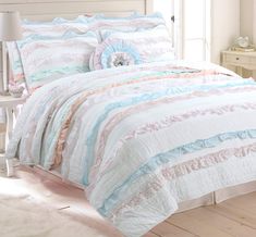 a white bed with blue and pink comforter on top of it next to a window