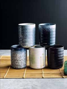 five black and white vases sitting on top of a bamboo mat next to each other