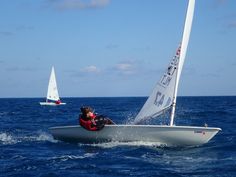 two people in a small sailboat on the ocean with one person sailing behind them