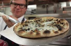 a man holding a pizza on top of a metal tray in front of an oven