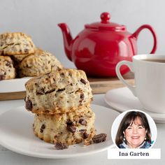 there are cookies on the plate next to a cup and saucer with a teapot in the background