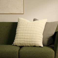 a green couch with two pillows on top of it and a painting above the couch