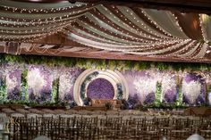 an indoor wedding setup with purple and white flowers, greenery and lights on the ceiling