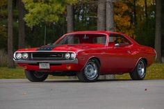 a red muscle car parked on the side of the road in front of some trees