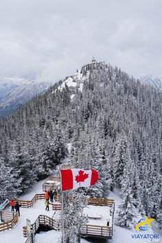 a canadian flag on top of a mountain with people standing around it and trees in the background