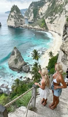 two women standing on steps looking at the water and cliffs in front of them with palm trees