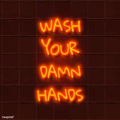 the words wash your damn hands are lit up in neon orange letters on a brick wall