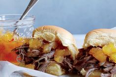 two pulled pork sandwiches with pineapple slaw on a white plate next to a jar of orange juice