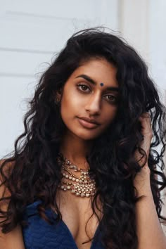 a woman with long dark hair wearing a blue dress and gold jewelry on her neck