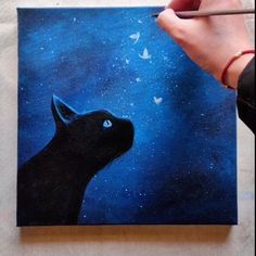 a person is painting a black cat with blue eyes and stars on the sky behind it