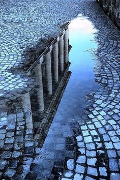 a reflection of a building in the water on cobblestone pavement with an umbrella