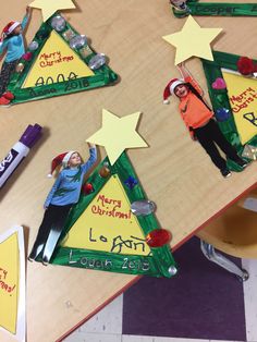 three christmas tree shaped magnets sitting on top of a wooden table next to markers and pencils