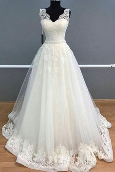 a white wedding dress on a mannequin stand in front of a gray wall