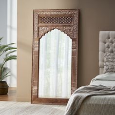 a bed sitting next to a tall mirror in a bedroom