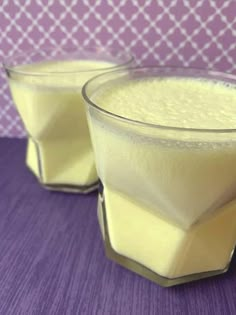 two glasses filled with white liquid sitting on top of a purple tablecloth next to each other