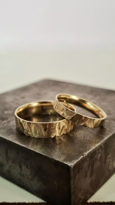 two gold wedding rings sitting on top of a box