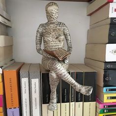 a statue sitting on top of a pile of books in a room filled with stacks of books