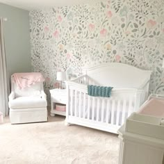 a baby's room decorated in pastel colors and floral wallpaper, including a white crib