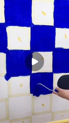 a person painting a wall with blue and white squares on the walls, while holding a paint roller in their hand