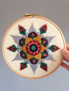 an embroidered flower on a white wall hanging from a wooden hoop with two gold hooks