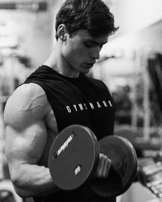 a man holding two dumbs while standing in a gym with one arm behind his back