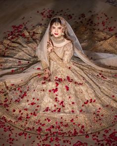 a woman in a white and gold wedding dress with rose petals on the floor next to her