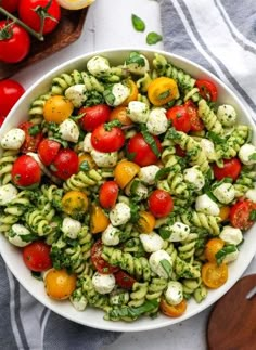 a white bowl filled with pasta salad next to tomatoes and broccoli on a wooden cutting board