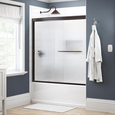 a bathroom with blue walls and white towels hanging on the shower door, next to a window