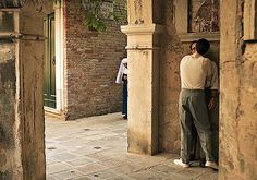 a man standing in an alley between two buildings with people walking around them and looking at something on the ground