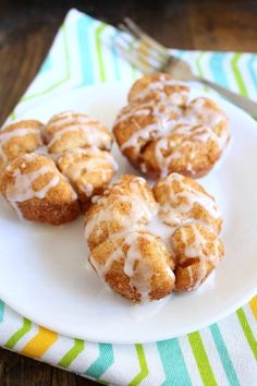 three donuts with icing on a white plate next to a fork and napkin