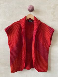 a red cardigan hanging on a white wall with a pink ball in the corner