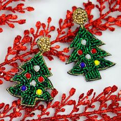 two christmas tree shaped earrings sitting on top of red sequins