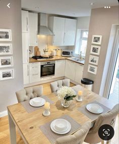 a dining room table with place settings and pictures on the wall behind it in front of an open kitchen door