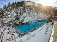 an aerial view of a swimming pool surrounded by snow covered trees and mountains in the background