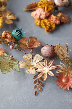 an arrangement of leaves, flowers and eggs on a gray surface with one egg in the center