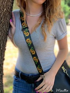 a woman holding onto a tree wearing a sunflower lanyard and carrying a black purse