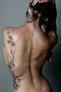 the back of a woman's body with flowers tattooed on her upper and lower half