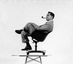 a black and white photo of a man sitting on a chair with a pipe in his mouth