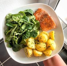 a white plate topped with potatoes, spinach and salmon