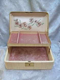 an old wooden box with pink flowers painted on it's lid and inside is sitting on a white cloth