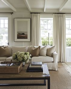 a living room filled with furniture and windows covered in white drapes, along with a coffee table