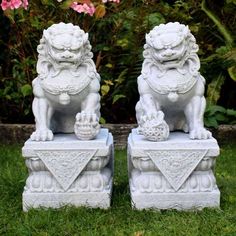 two white stone lions sitting on top of each other in the grass next to flowers