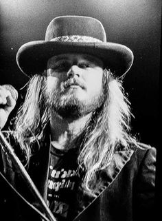 a man with long hair wearing a hat and holding a microphone in his right hand